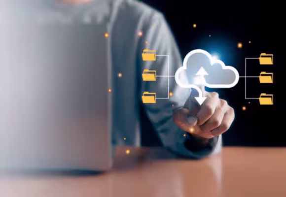 Une personne sur un ordinateur portable pointant son doigt sur un logo 'cloud' en relief. Ce logo est relié à plusieurs fichiers en relief aussi.